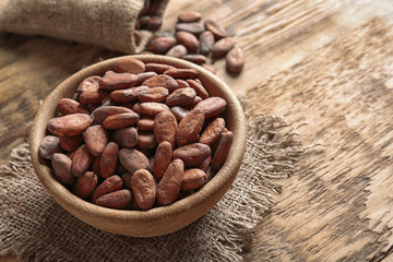 Bowl with aromatic cocoa beans on wooden table