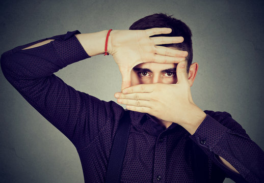 Young man peeking through his fingers hands