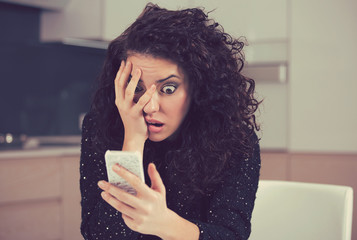 Shocked anxious woman looking at phone seeing bad news message