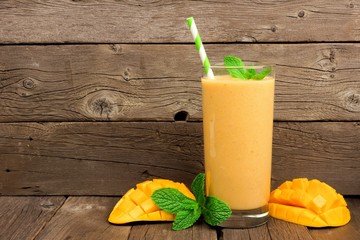 Healthy mango smoothie in a glass with mint and straw against a rustic wood background