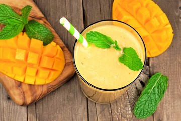Healthy mango smoothie in a glass, overhead scene on a rustic wood background