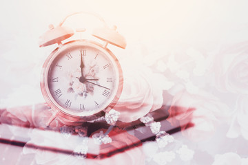 vintage alarm clock on a book blended with roses background, filtered tones