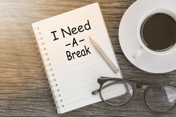 Concept I need a break message on notebook with glasses, pencil and coffee cup on wooden table.