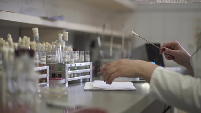 Hands of female technician during microbiology and bacteriology analysis, dolly macro shot  through the glassware, shallow depth of field, room interior