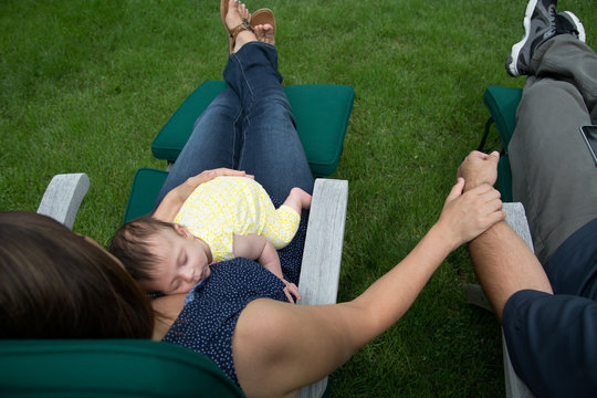 baby sleeps on mother's chest while mother and father sit outside