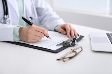 Close-up of a female doctor filling  out application form , sitting at the table in the hospital