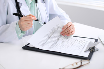Fototapeta premium Close-up of a female doctor filling out application form , sitting at the table in the hospital