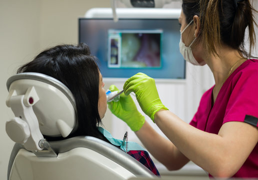 Dentist at work examining woman's teeth in dental clinic with remote camera. Picture of teeth is on the screen. New dental technologies.