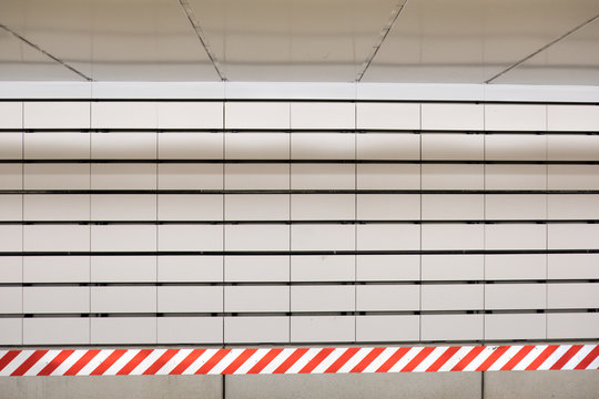 White Subway Tile And Red And White Striped Caution Sign Or Tape In A New York City Subway Station.  New York Underground Train Station, Wall Of White Tiles, Low Ceiling, Head On Shot.