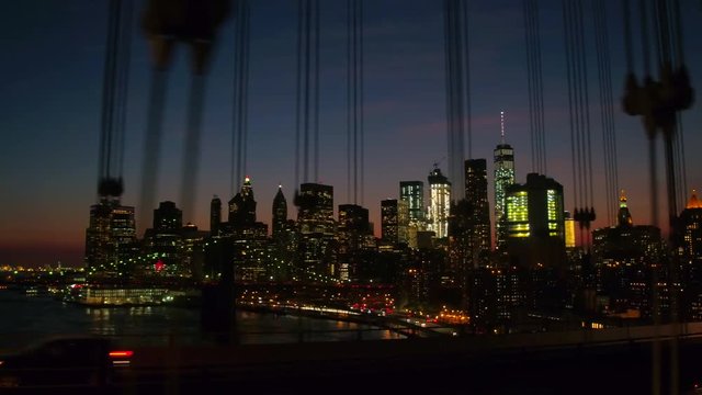 CLOSE UP: Driving over Manhattan Bridge overlooking iconic Brooklyn Bridge interchange on interstate highway and contemporary glassy skyscrapers illuminated with city lights in NYC downtown at night