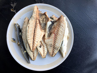 mackerel in white dish on black background.