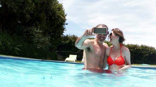 Happy couple taking selfie from mobile phone in pool
