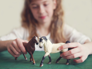 The girl is playing with the figures of horses. 