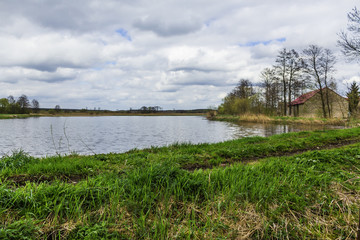 Fish pond in the spring in the middle of April. Green grass on the shore. A fisherman's house in the background. Podlasie, Poland.