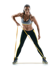 Athletic young girl performs exercises using a resistance band and looking at the camera. Photo of...
