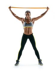 Young girl performs exercises for the muscles of the back and hands using a resistance band and looking at the camera. Photo of athletic girl isolated on white background. Strength and motivation.