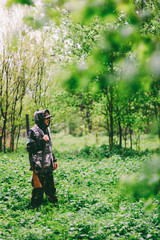 A man hunter wanders with a gun in rainy weather through a spring forest, toned photo