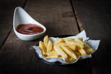 Traditional French fries with ketchup on rustic wooden background.