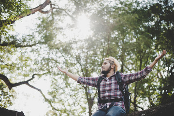 Young hiker hipster man sitting raising her arm on branch with backpack, Travel concept.