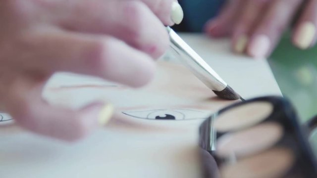 Face sculpting - training on the face-chart. Young woman in a bright studio draws a facechart. The make-up artist draws a schematic image of a face on watercolor paper and applies make-up.
