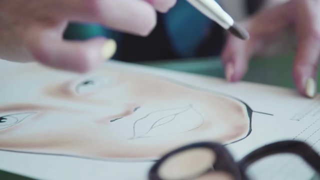 Make-up artist creates a make-up sketch on the face chart. Inspiration: make-up artist draws face-lines on watercolor paper, using professional cosmetics. Face sculpting - training on the face-chart.