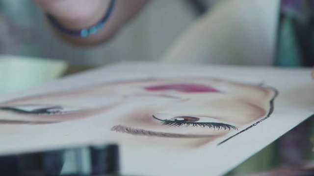 Face chart: the make-up artist draws eyelashes with eyeliner. The make-up artist draws a schematic image of a face on watercolor paper. Woman make-up artist learns to apply make-up using the face map.