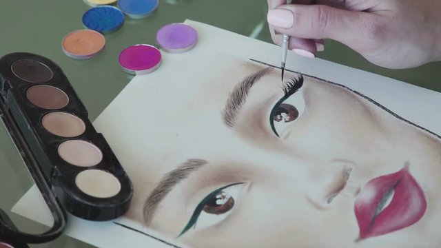 Young woman in a bright studio draws a facechart. Close-up: the make-up artist draws the eyelashes on the face chart. A woman make-up artist learns to apply make-up using the face map.