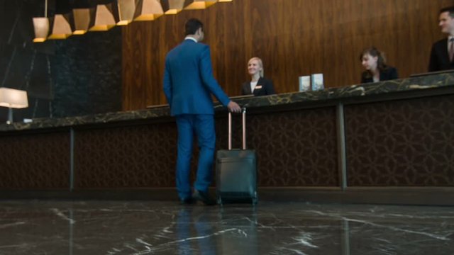 Businessman with suitcase walking to reception desk
