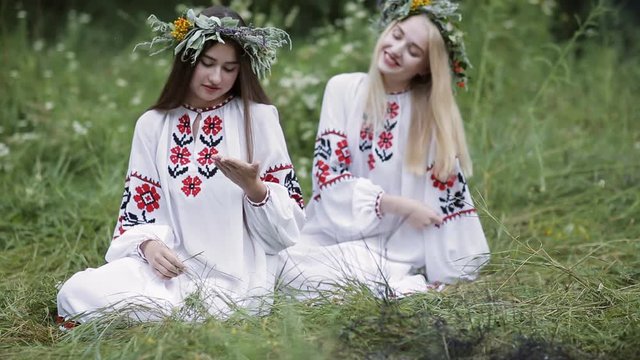 Midsummer. Two girls in Slavic clothes talking while sitting by the fire