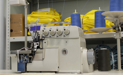 new overlock machine for the textile industry in the background of shelves with knitted and sewn products.