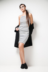 Fototapeta premium Attractive young woman looking at camera standing in elegant clothes. Vertical studio shot.