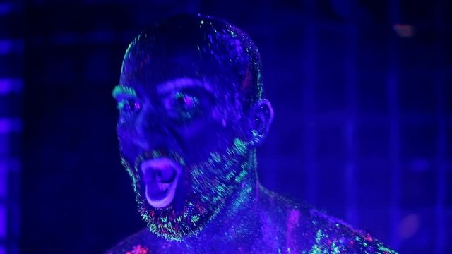 man painted fluorescent powder dance and grimaces in ultraviolet light