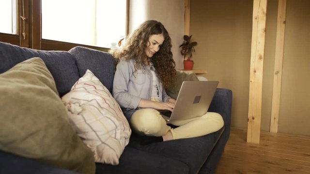 Beautiful teenage girl at home sitting on couch working on laptop.