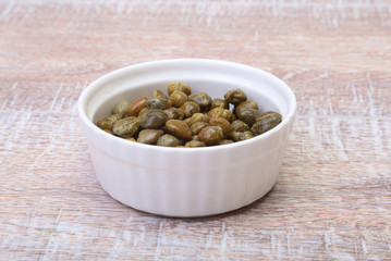 bowl with fresh capers on wooden table