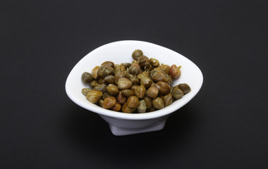 bowl with fresh capers isolated on black background.