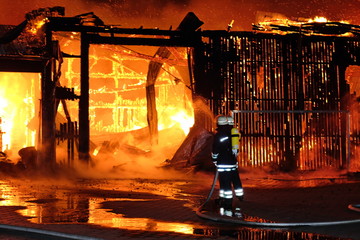 Großbrand einer Halle mit heftigem Feuer und Löscharbeiten der Feuerwehr.