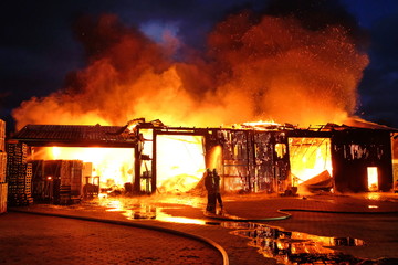 Großbrand einer Halle mit heftigem Feuer und Löscharbeiten der Feuerwehr.