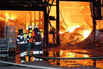 Fototapeta premium Großbrand einer Halle mit heftigem Feuer und Löscharbeiten der Feuerwehr.