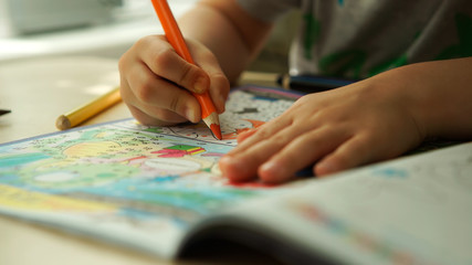 Child hands paints a orange pencils on a paper
