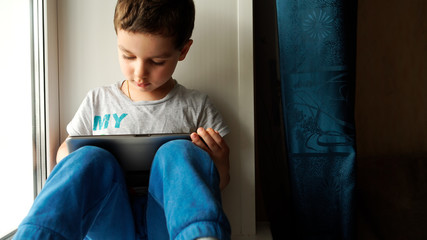 Child sits on a windowsill and uses a digital tablet pc