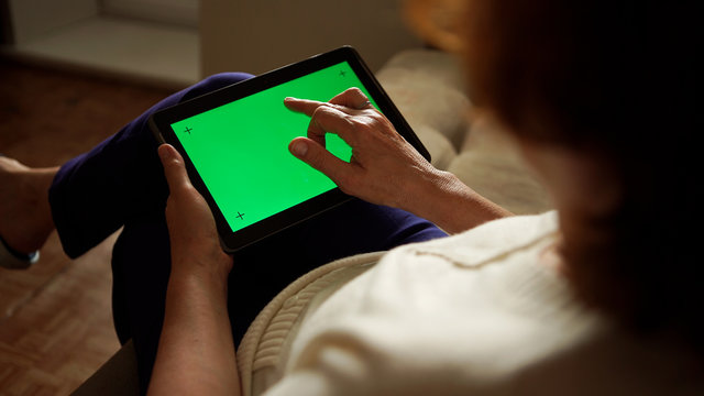 Aged Woman Using A Digital Tablet PC With Green Screen, Back View