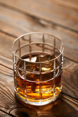 Glass of whiskey with ice cubes on wooden table