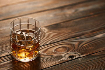 Glass of whiskey with ice cubes on wooden table