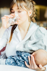 Vertical porttrait of young charming mother drinking water while breast feeding baby boy