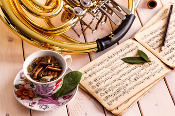 French horn on light wooden background. Musical background – French horn, tea, notes.