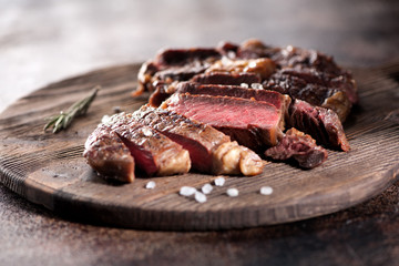 Ribeye steak slices with salt and rosemary on a wooden serving board