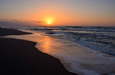 Fototapeta na wymiar Amanecer en la playa, observándose en el horizonte la salida del sol y un bonito cielo con diferentes tonalidades que se reflejan en el agua de la orilla del mar