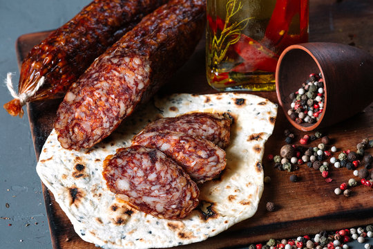 Smoked salami with pita and spices on a wooden cutting board on dark background