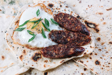 Pita with fried egg and pieces of salami on a wooden cutting board on grey background
