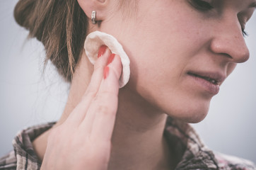 A young woman applies a cotton ball to her face